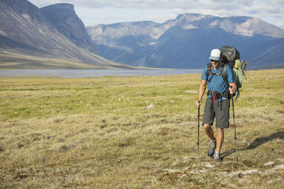 Backpacker trekking through open alpine meadow in river basin.