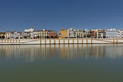 Buildings by river against clear blue sky