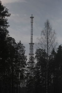 Low angle view of telecommunications tower in wood against cloudy sky