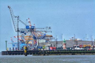 Cranes at harbor against sky