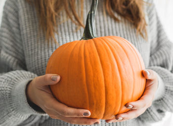 Midsection of woman holding pumpkin during autumn