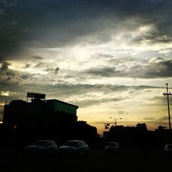 Cars on road against cloudy sky at sunset