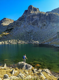 Rear view of person on rock by lake against sky