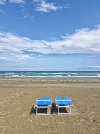 Empty deck chairs at beach against sky