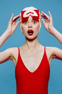 Portrait of young woman with arms raised against blue background