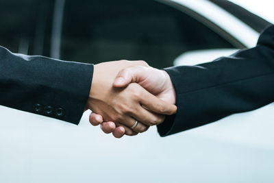 Cropped image of business colleagues shaking hands against car