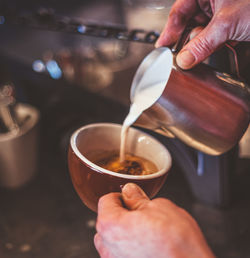 Cropped hands of person pouring milk in coffee cup