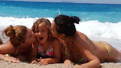 Women in bikini kissing girl while lying at beach