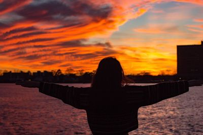 Rear view of silhouette woman standing by sea against orange sky