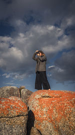 Low angle view of woman standing on rock against sky