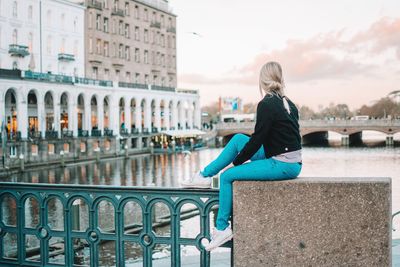 Young woman sitting on railing against sky