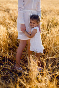 Daughter hugging mother's leg on yellow wheat field evening in summer