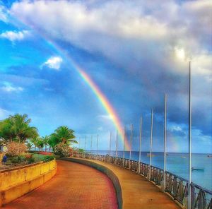 Rainbow over road against cloudy sky