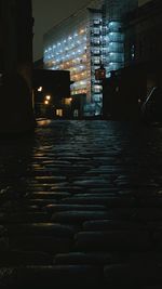 Surface level of wet street amidst buildings at night