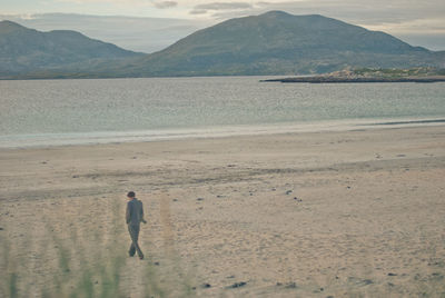 Rear view of a man walking on calm beach