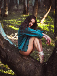 Young dancer sitting on tree trunk in forest