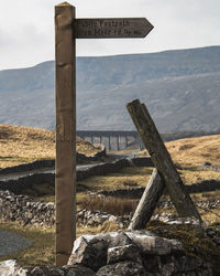 Wooden post on field by mountains against sky