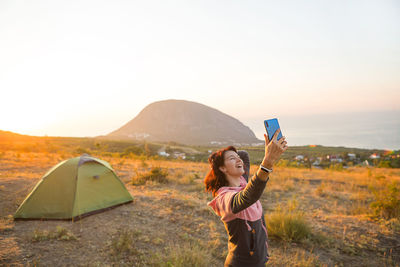 Woman takes photos of the sunrise in the mountains on her phone. selfie in rising sun. panoramic 