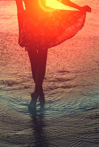 Low section of woman standing on beach during sunset