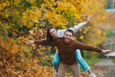 Smiling woman with arms outstretched against trees during autumn