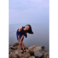 Portrait of happy woman bending on rocks by sea