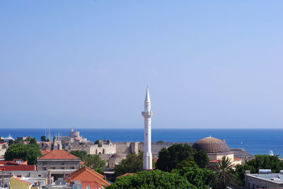 Buildings by sea against clear blue sky