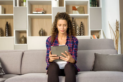 Young woman using phone while sitting on sofa at home