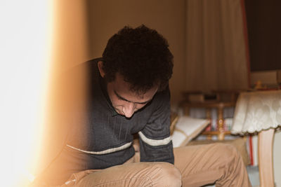 Man looking away while sitting on chair at home