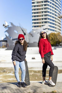 Portrait of teenage girls with skateboard standing in city