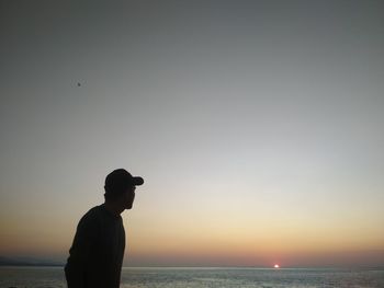 Silhouette man looking at sea against sky during sunset