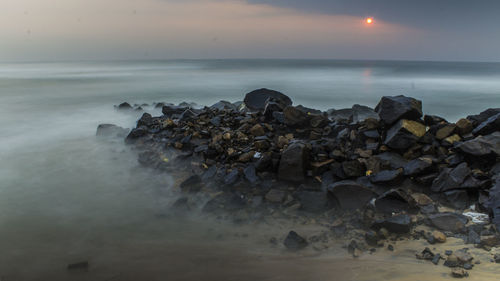 Rocks on beach against sky during sunset