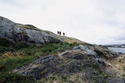 People on rocks by mountain against sky