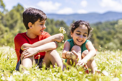 Smiling sibling picking flowers while sitting on land