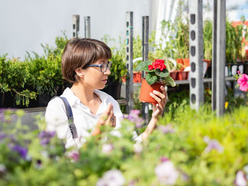 Woman chooses plants for landscaping. outdoor shelves with seedlings, plants in flower shop. 