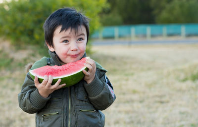 Boy eating watermelon while standing at park