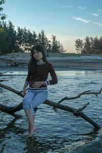 Portrait of young woman standing against trees at sunset