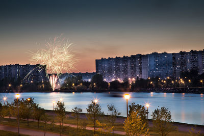 Firework display over river against sky in city at night