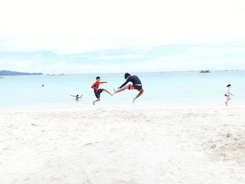 Teenagers playing on beach against sky