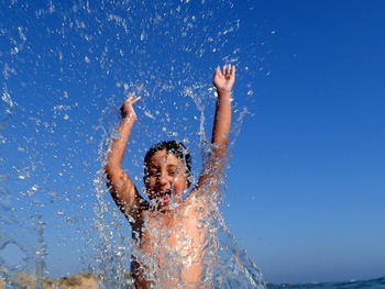 Close-up of shirtless boy splashing water against clear sky