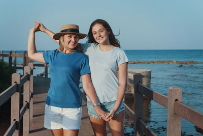 Mother and daughter standing on wooden walkway by the sea