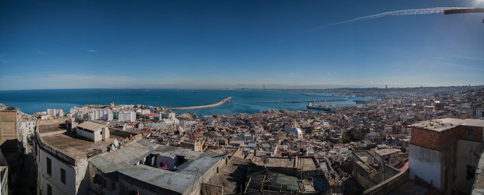 High angle view of townscape by sea against blue sky