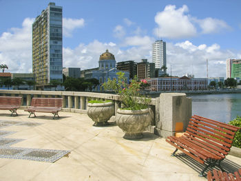 City building and empty bench at lakeside