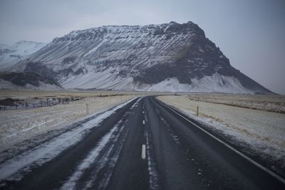 Country road leading towards snowcapped mountains against sky