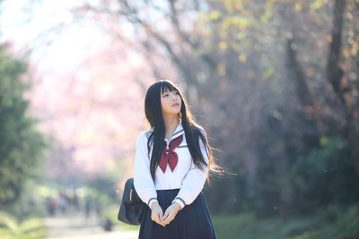 Woman looking away while standing against trees