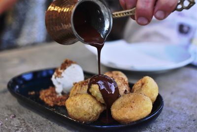 Cropped hand pouring chocolate on dessert served in plate on table