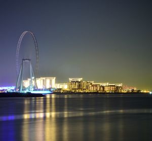 Illuminated city by river against sky at night