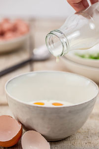 Cropped hand of person pouring milk in bowl on table