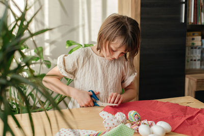 A girl at home prepares fabric for making easter textile eggs in the shape of a hare with ears.
