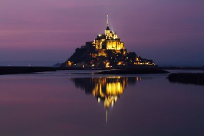 Illuminated mont saint-michel on sea against sky at dusk