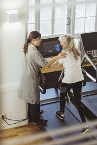 Female nurse assisting elderly woman exercising on treadmill in nursing home